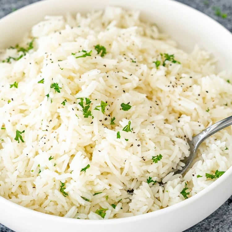 a white bowl with perfectly cooked jasmine rice garnished with some parsley.