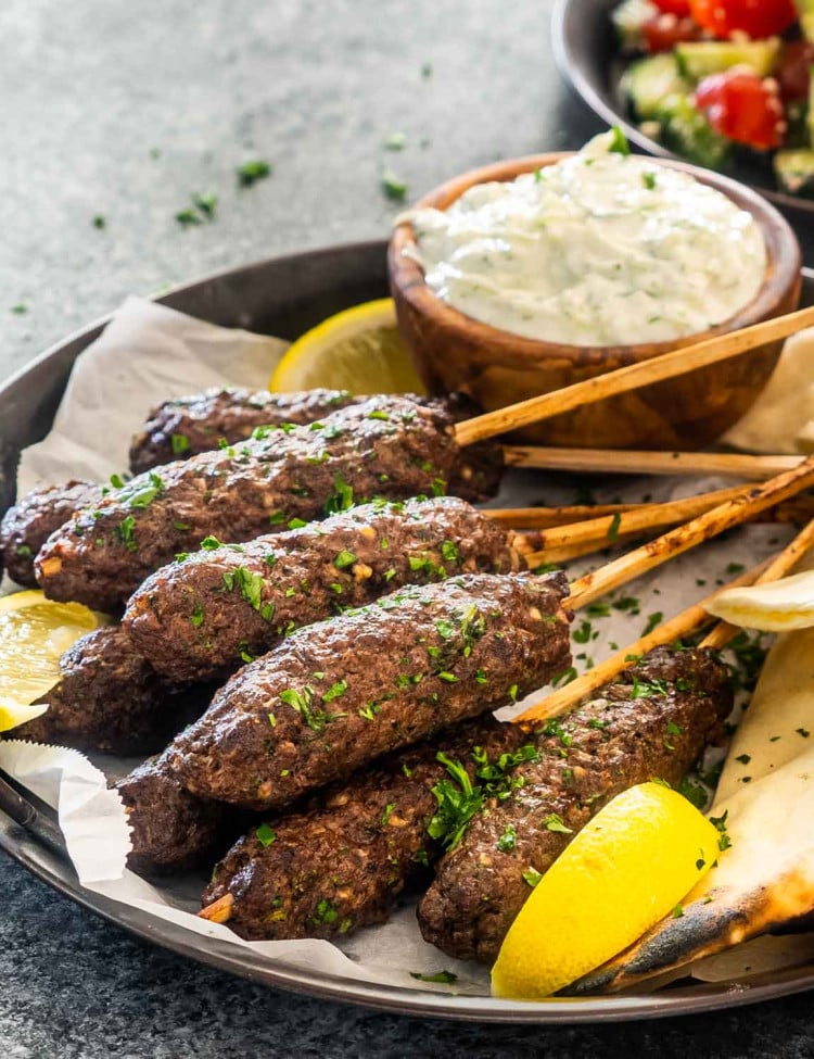 a few beef koftas on a plate with some pitas garnished with parsley next to tzatziki sauce.