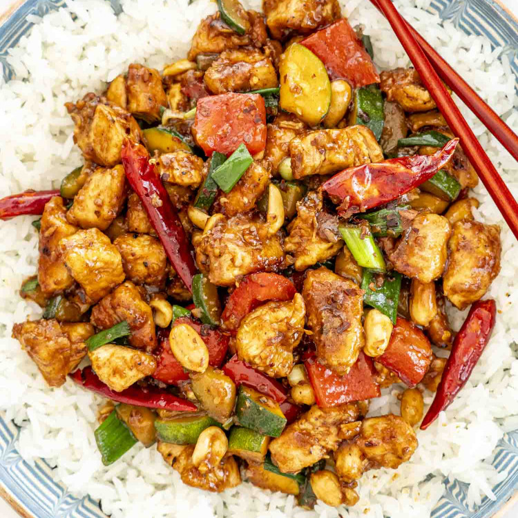 kung pao chicken over a bed of rice with 2 chopsticks.