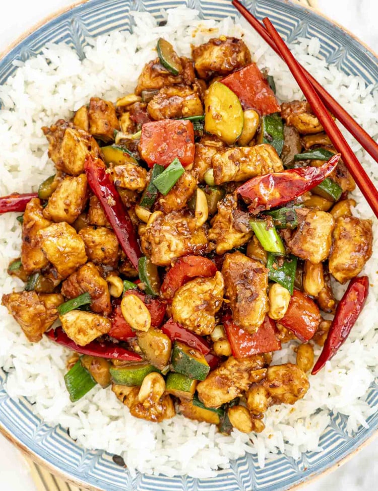 kung pao chicken over a bed of rice with 2 chopsticks.