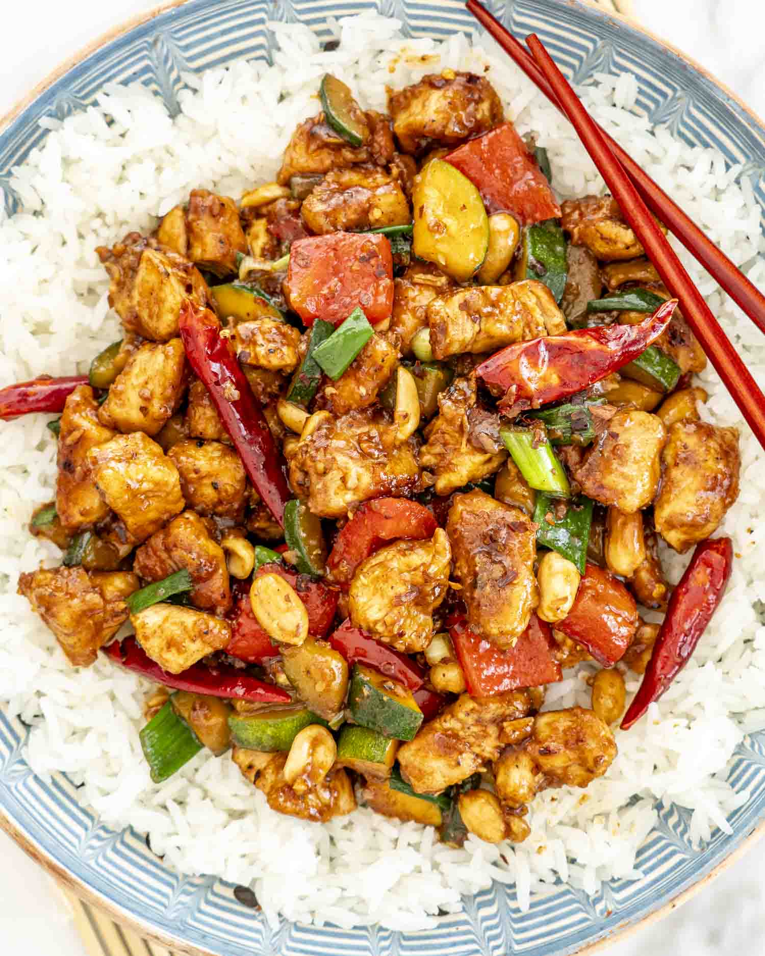 kung pao chicken over a bed of rice with 2 chopsticks.