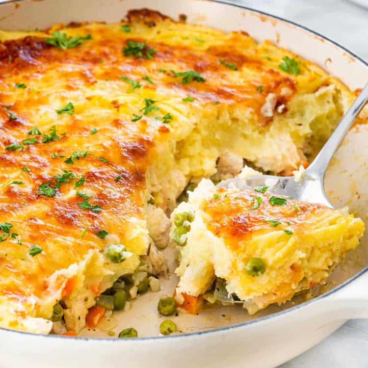 closeup shot of leftover turkey shepherd's pie in a skillet with a serving spoon.