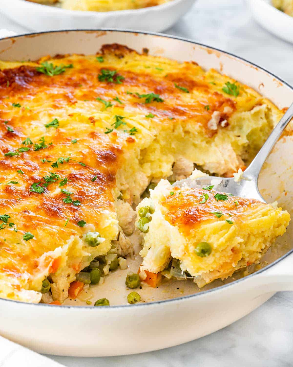 closeup shot of leftover turkey shepherd's pie in a skillet with a serving spoon.