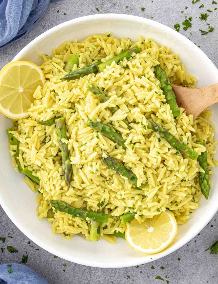 lemon orzo and asparagus in a white bowl garnished with lemon slices.