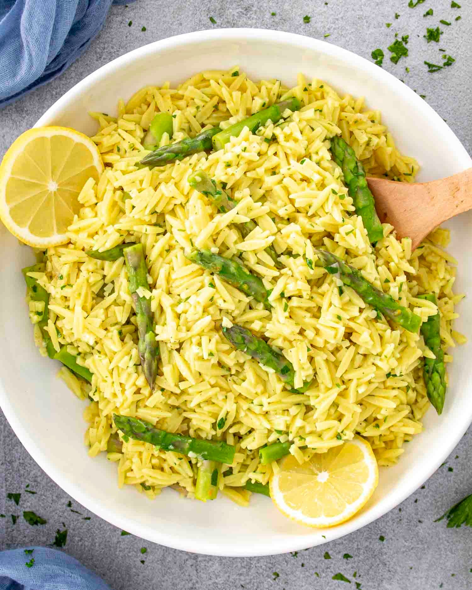 lemon orzo and asparagus in a white bowl garnished with lemon slices.