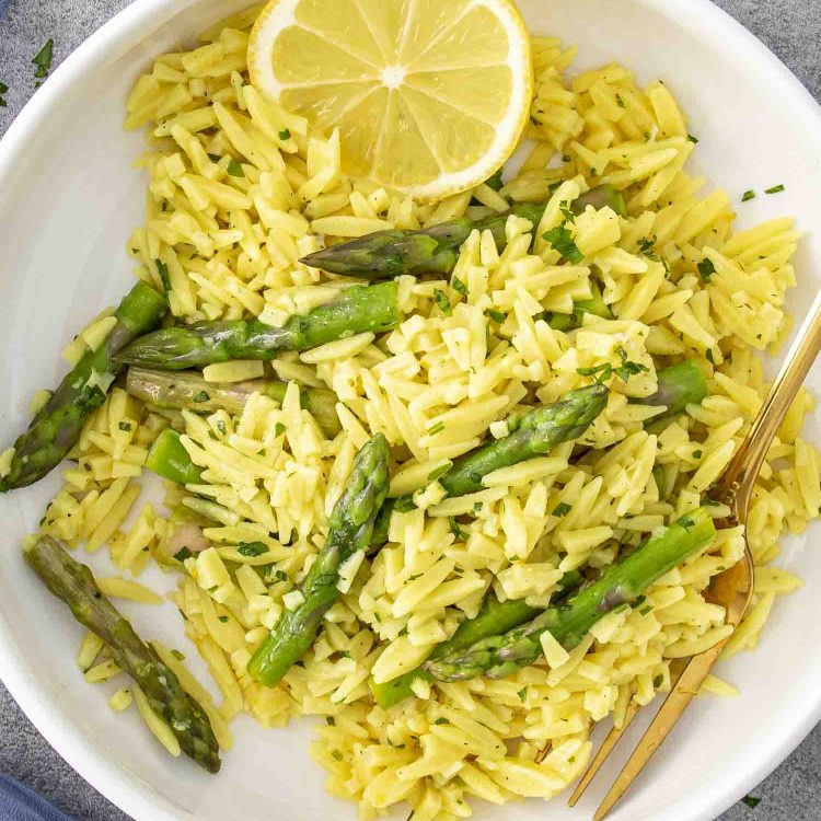 lemon orzo and asparagus in a white bowl garnished with lemon slices.