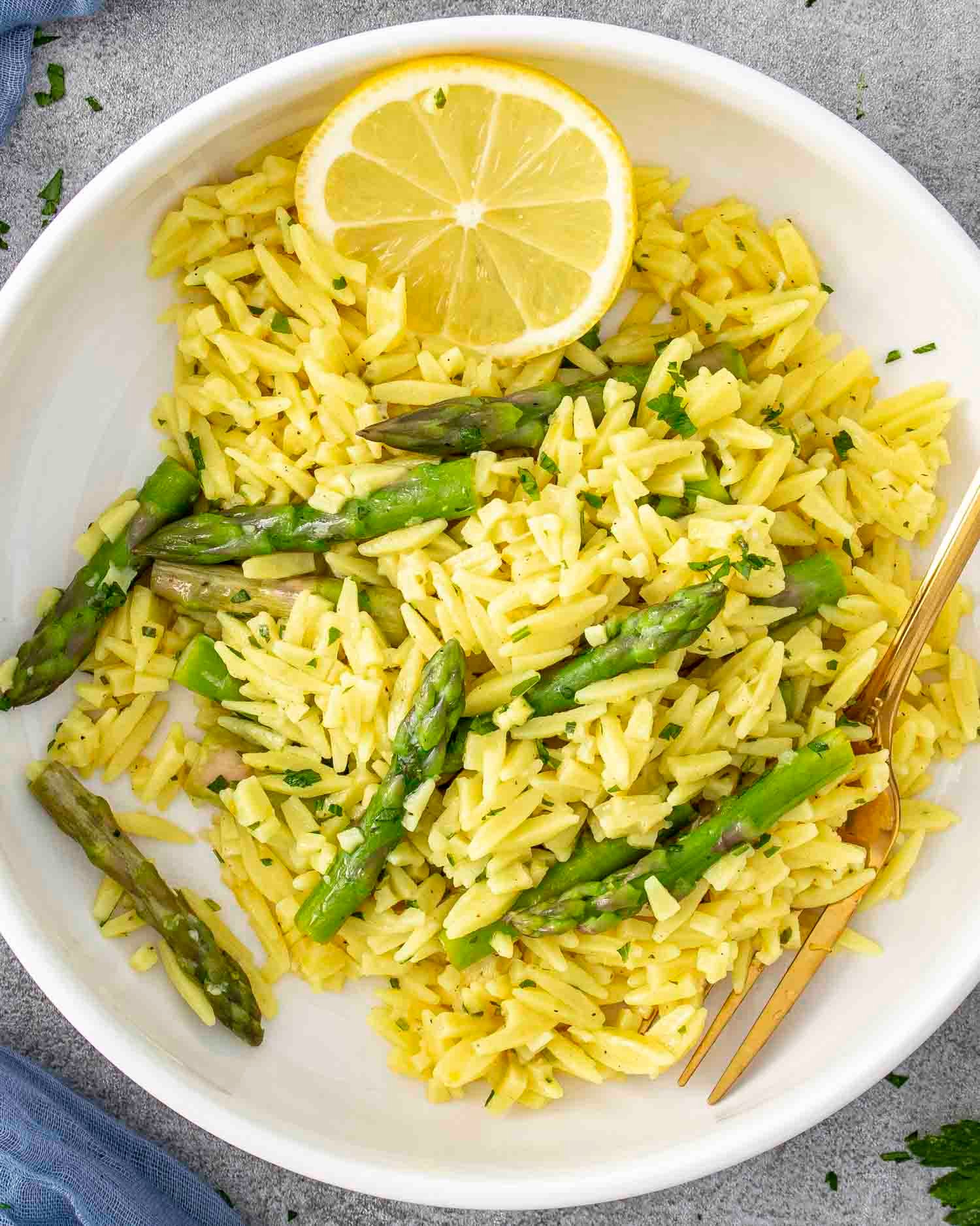 lemon orzo and asparagus in a white bowl garnished with lemon slices.