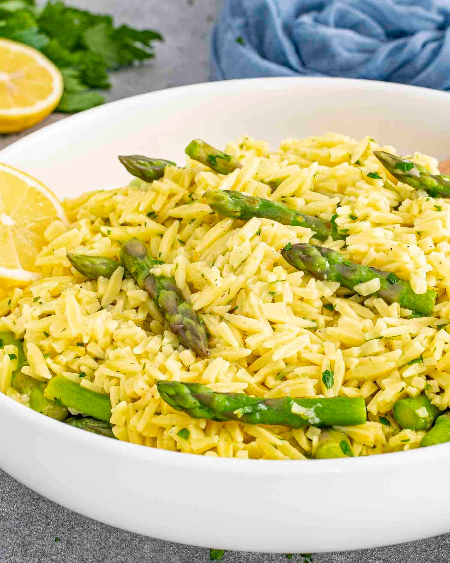 lemon orzo and asparagus in a white bowl garnished with lemon slices.