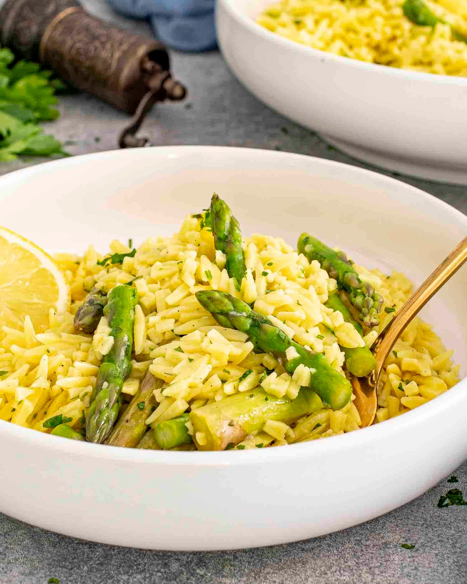 lemon orzo and asparagus in a white bowl garnished with lemon slices.