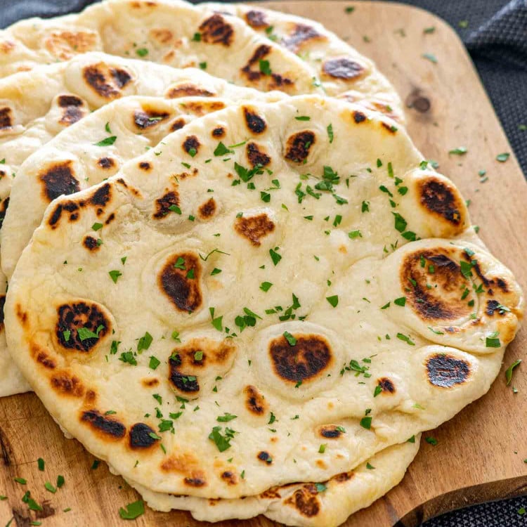 a stack of naan bread on a cutting board garnished with parsley.