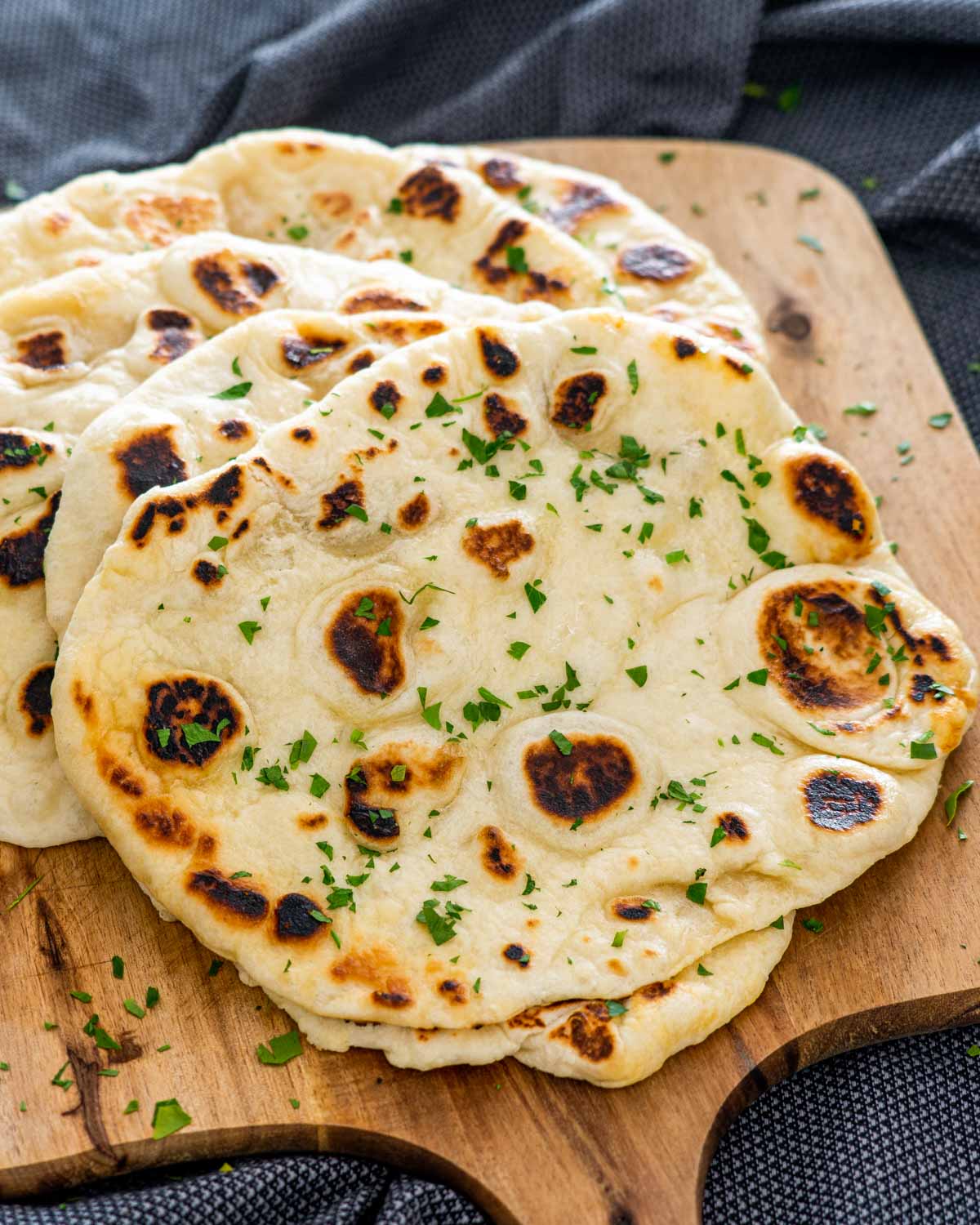 a bunch of naan on a cutting board garnished with parsley.