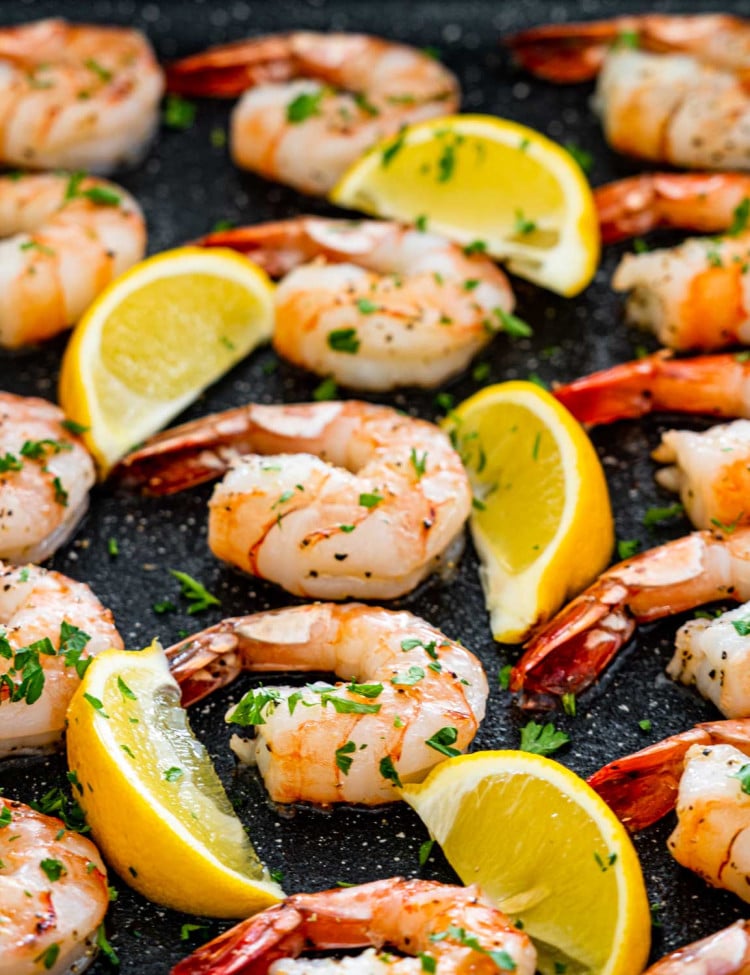 oven baked shrimp in a casserole dish with lemon wedges.