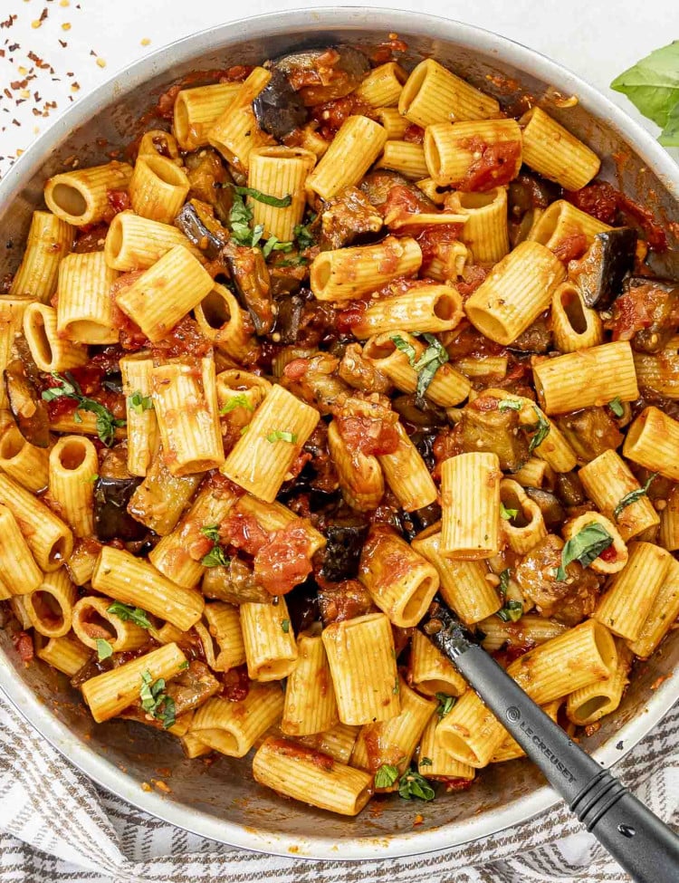 A skillet of Pasta alla Norma featuring rigatoni in a rich tomato sauce with tender eggplant chunks, garnished with fresh basil.