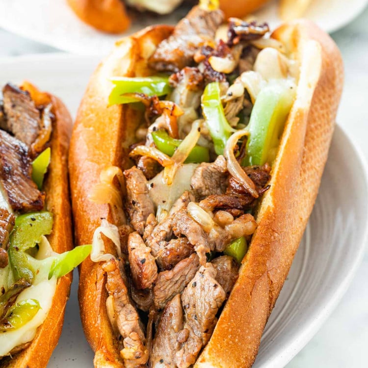 closeup of a philly cheesesteak sandwich on a white plate.