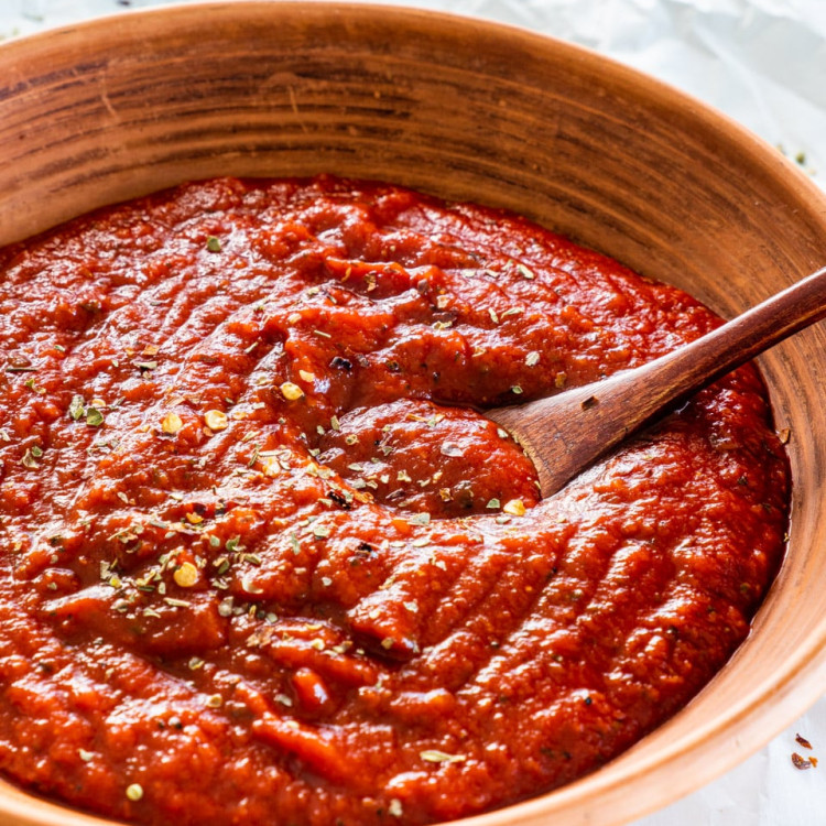 side shot of homemade pizza sauce in a brown plate with a mini wooden spoon in it