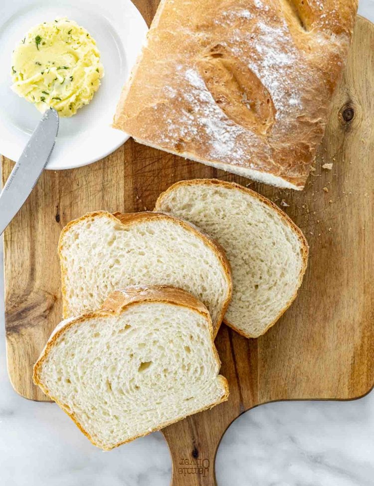 overhead shot of freshly made potato bread on a cutting board with 3 slices a plate with a pat of butter.