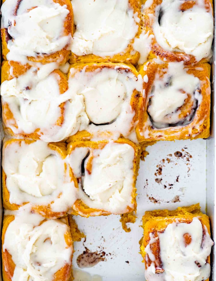 pumpkin cinnamon rolls with cream cheese icing in a baking pan.