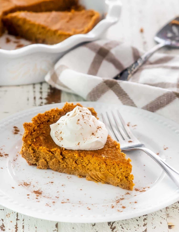 a slice of pumpkin pie with graham cracker crust topped with whipped cream.