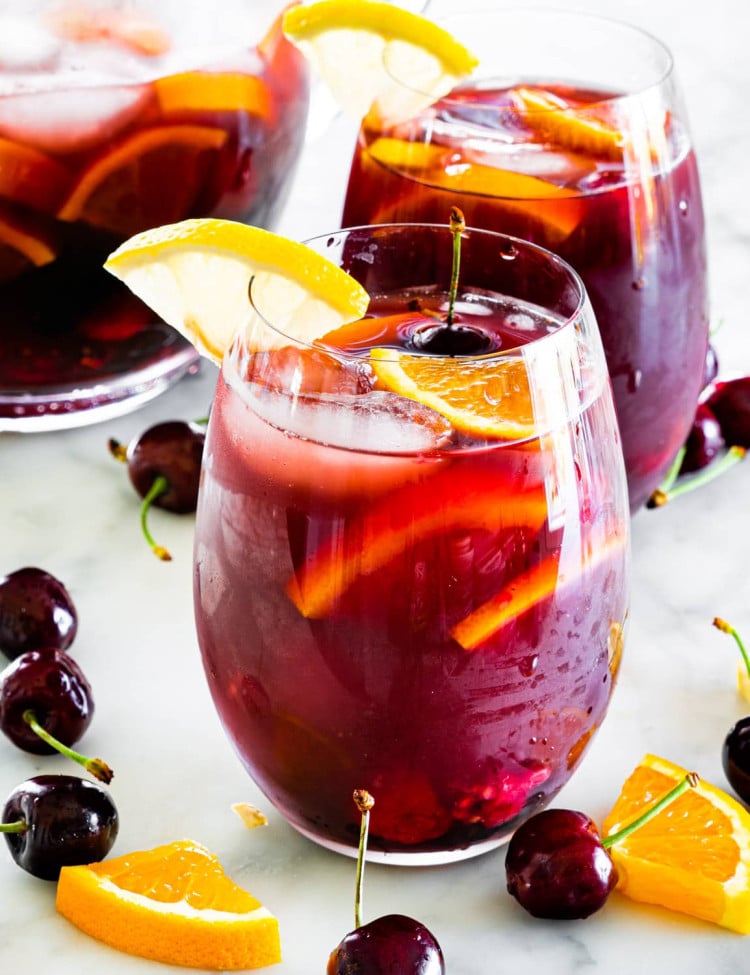 sideview shot of 2 glasses filled with red sangria and a pitcher in the background