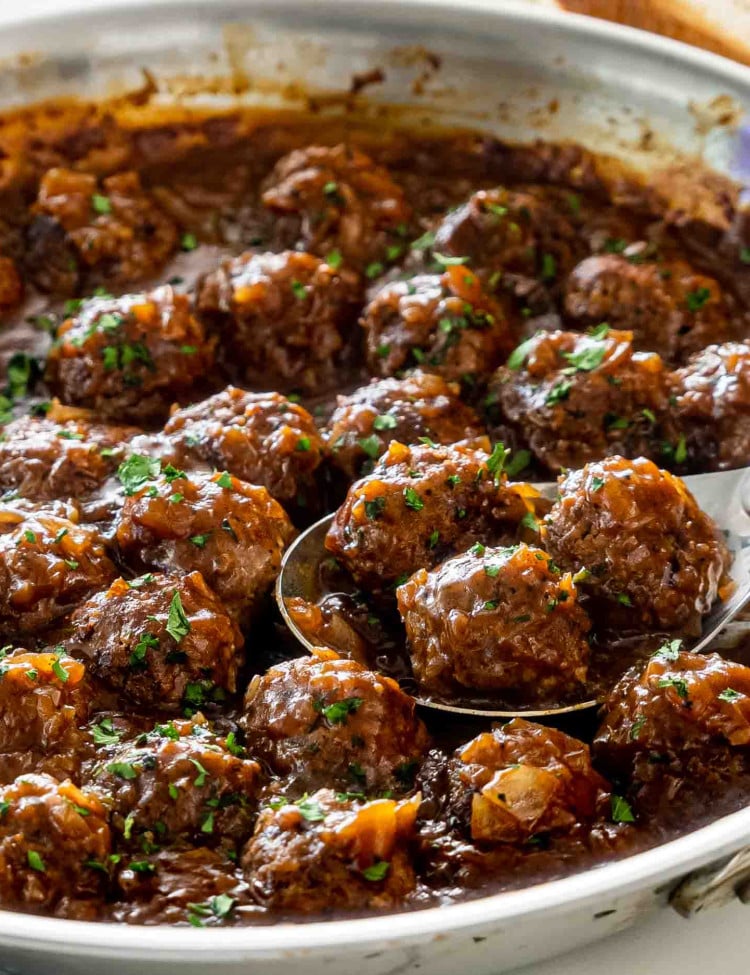 salisbury steak meatballs with gravy in a skillet garnished with parsley.