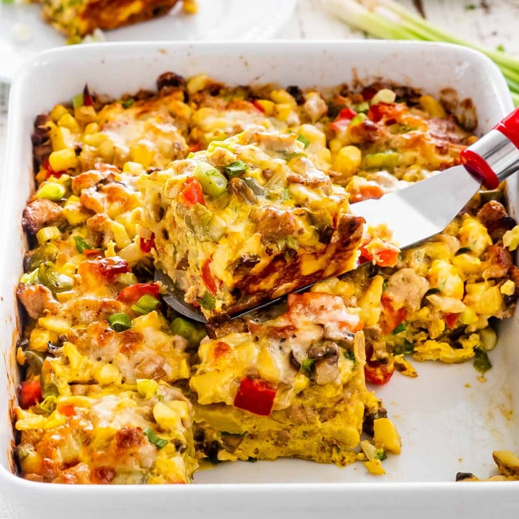 sausage potato breakfast casserole cut into slice with a spatula with a slice on top of the casserole.