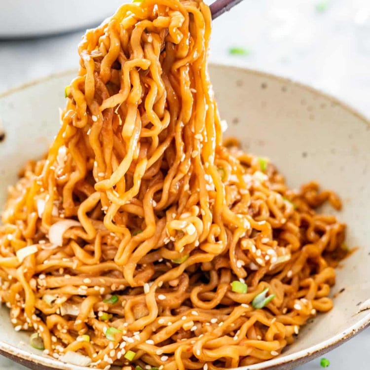 side view shot of chopsticks taking a bite of sesame noodles from a bowl