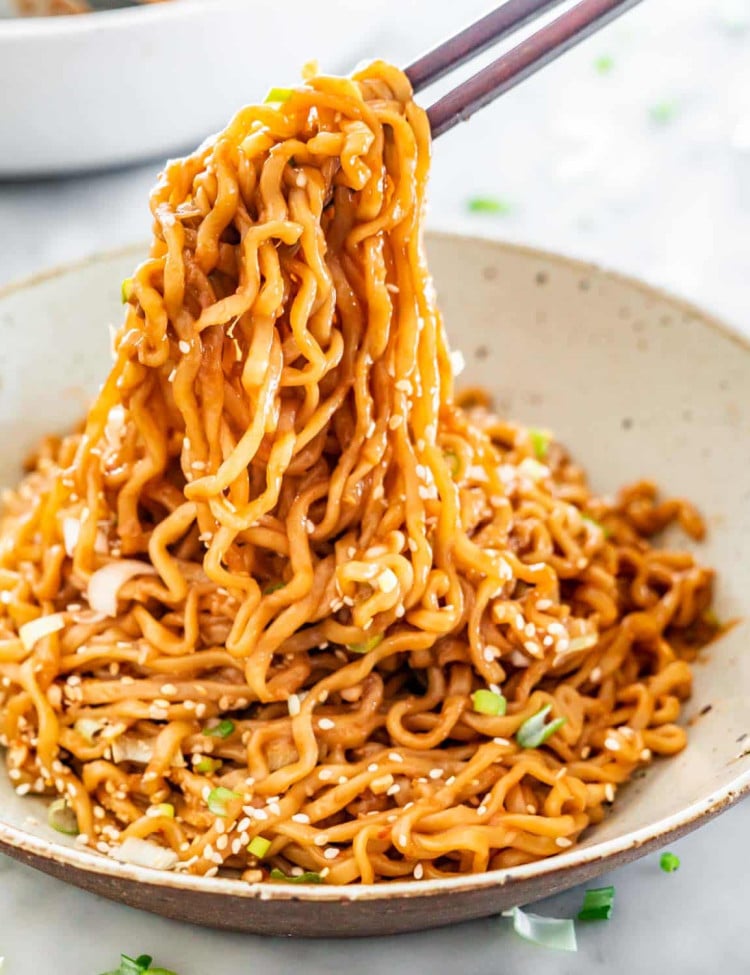 side view shot of chopsticks taking a bite of sesame noodles from a bowl