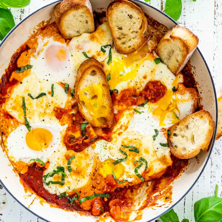 freshly made shakshuka in a beige skillet with some toasted bread.