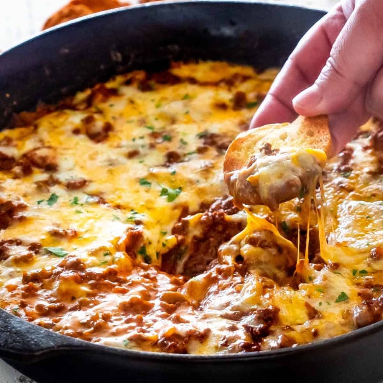 sloppy joe dip in a black skillet with a piece of toasted bread in it.