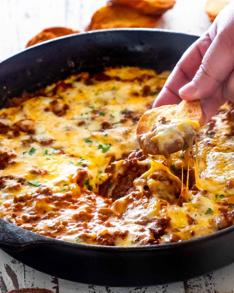 sloppy joe dip in a black skillet with a piece of toasted bread in it.