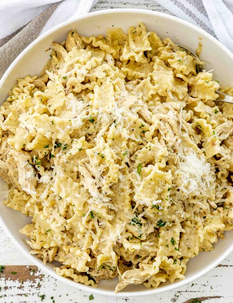 Bowl of slow cooker garlic Parmesan chicken pasta, topped with shredded Parmesan and parsley, ready to serve for dinner.