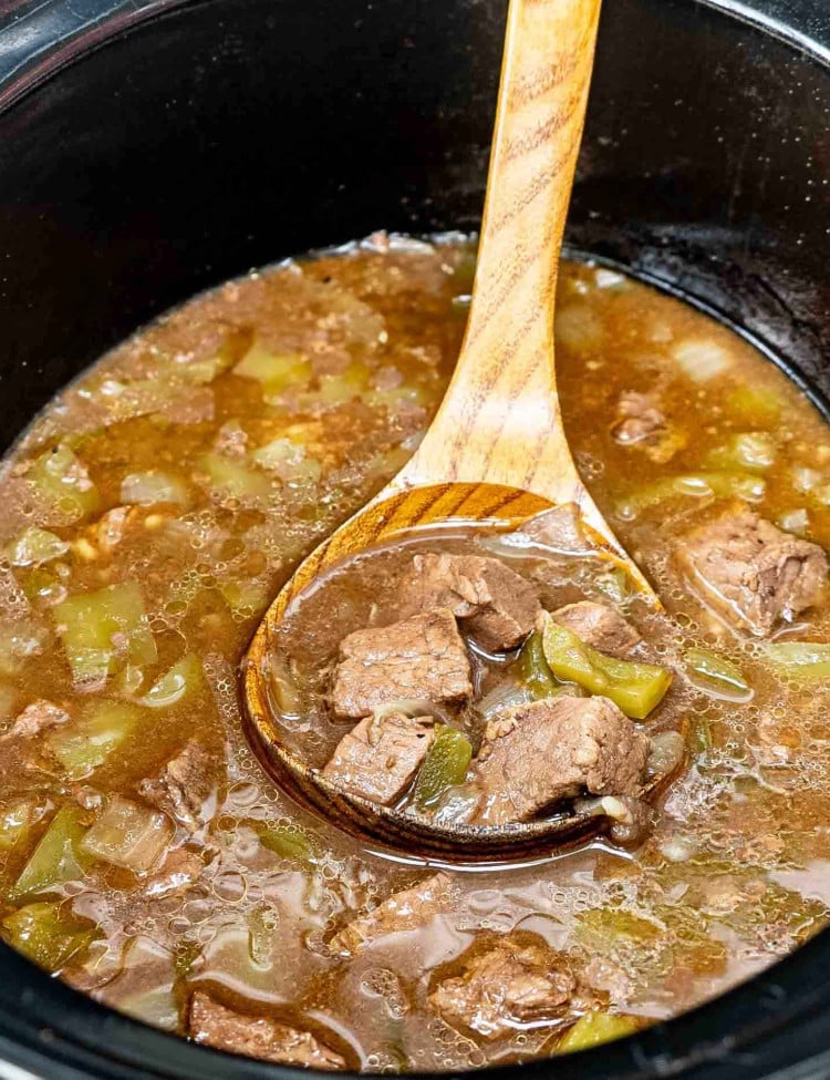 asian style pepper steak freshly made in a slow cooker with a wooden ladle inside.