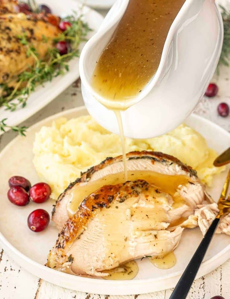 slow cooker turkey breast slices with gravy being poured over, served with mashed potatoes and cranberries.