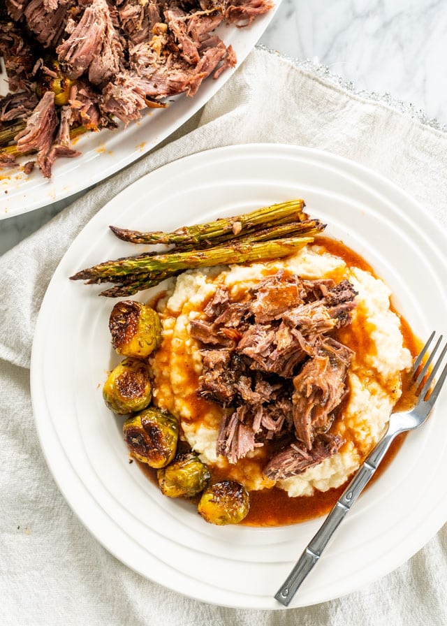 overhead shot of slow roasted leg of lamb on a plate with mashed potatoes brussel sprouts and asparagus