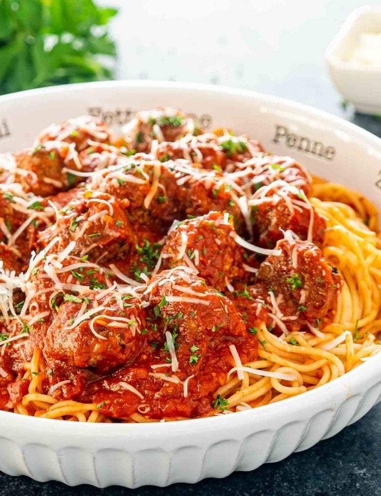 a white bowl full of spaghetti and meatballs garnished with parmesan cheese.