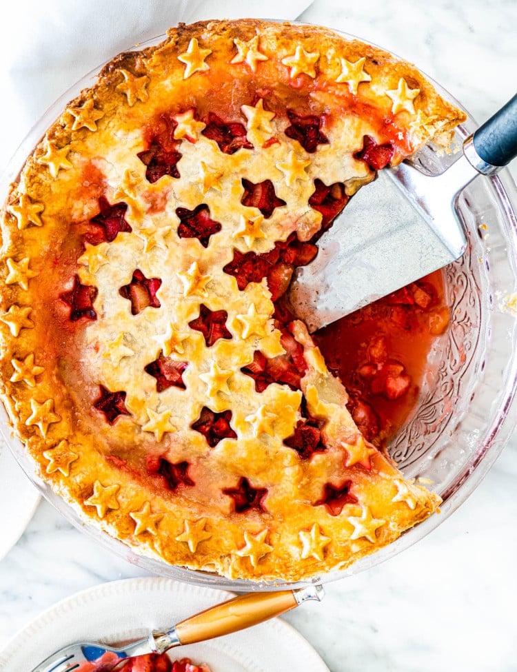 overhead shot of a strawberry rhubarb pie with two slices missing and a pie lifter sitting in the empty space