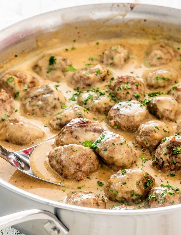 swedish meatballs with gravy in a skillet with a spoon in it.