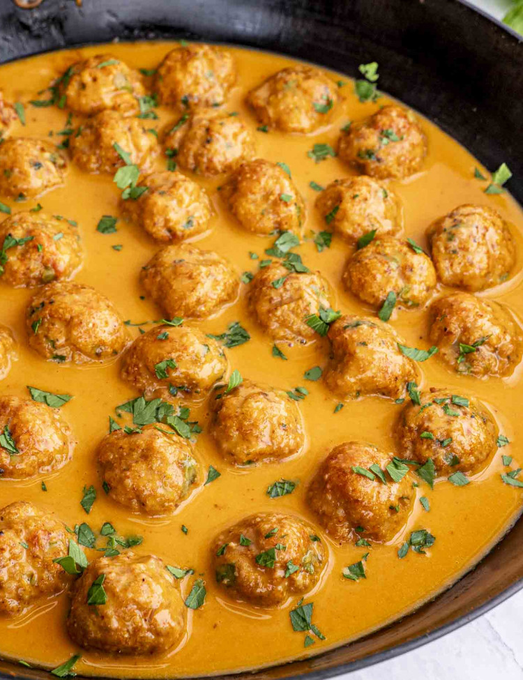 thai chicken meatballs with peanut sauce in a skillet garnished with cilantro.