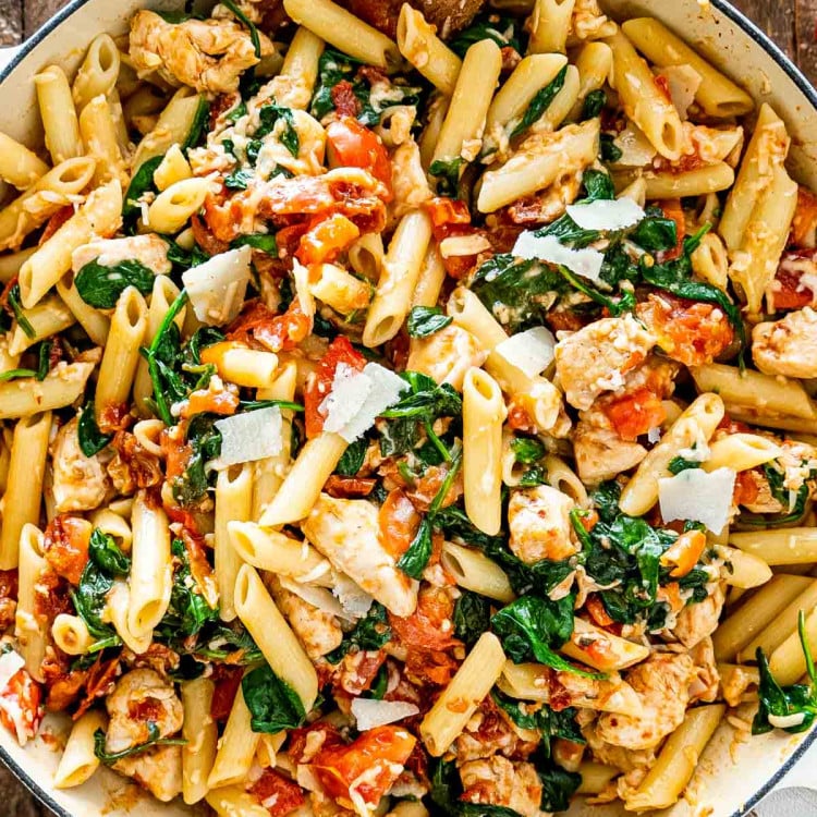 tomato spinach chicken pasta in a white bowl.