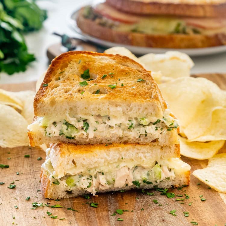 a tuna melt sandwich cut in two on a cutting board with potato chips.