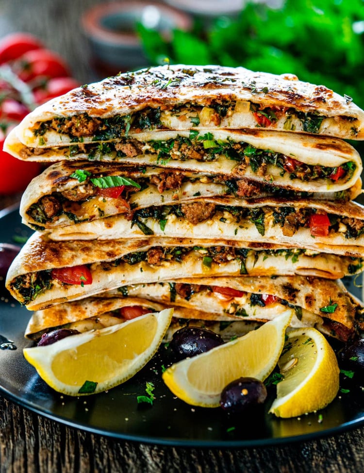 a stack of turkish gozleme on a plate with lemon wedges and olives as garnish