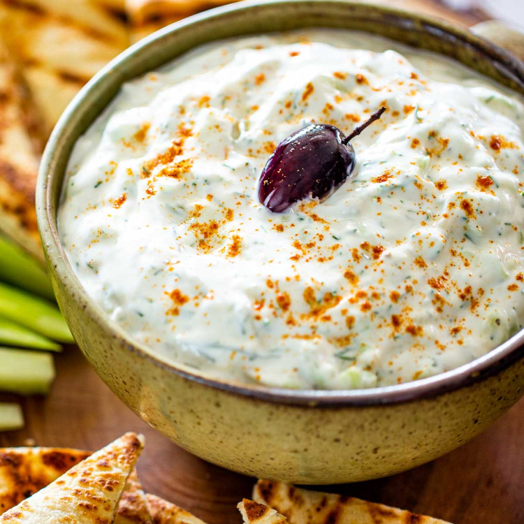 tzatziki sauce in a bowl with an olive on top surrounded by pita chips.