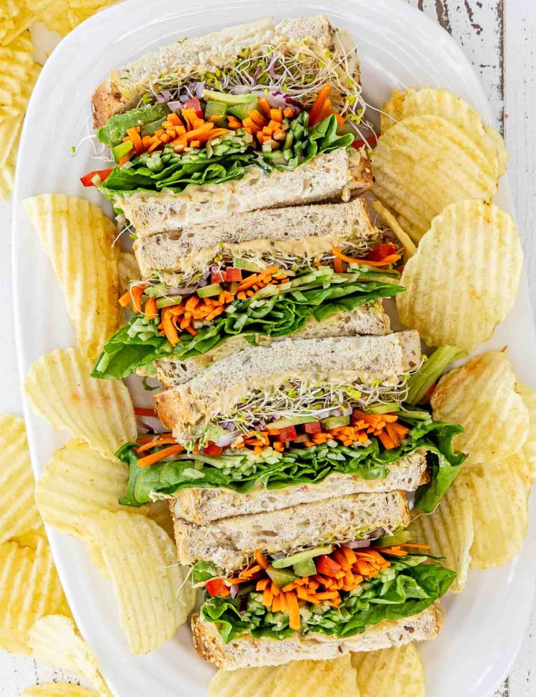 veggie and hummus sandwiches on a white platter along some potato chips.