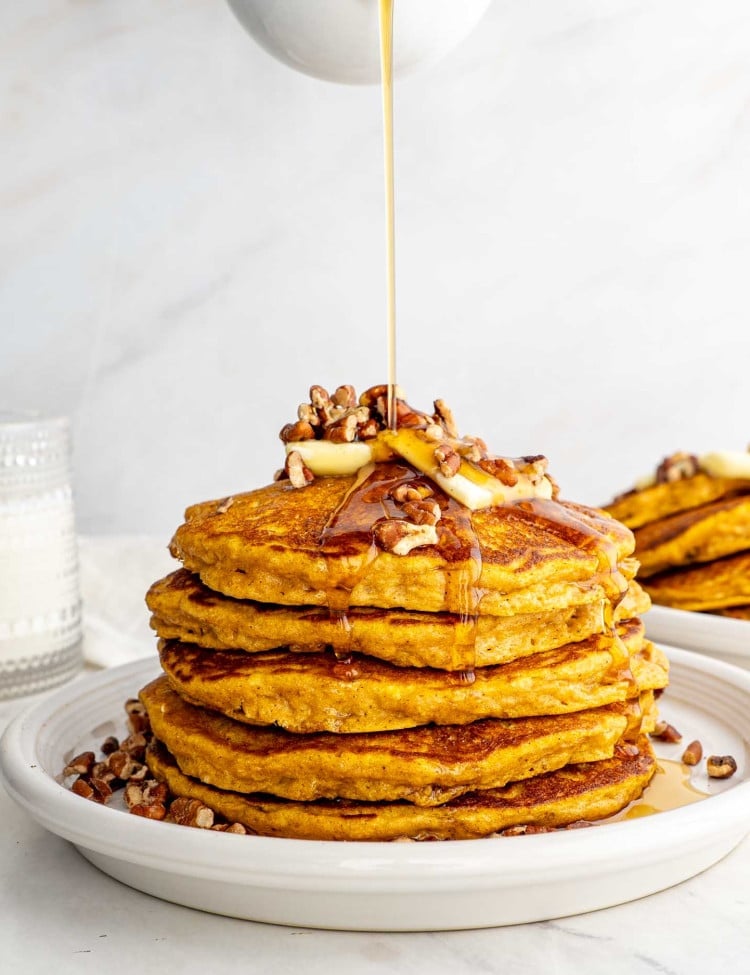 stack of whole wheat pumpkin pancakes on a white plate with pecans and a pat of butter.